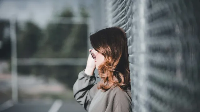 Frau lehnt an einer Wand und telefoniert lächelnd – vom Chat zum Telefonsex